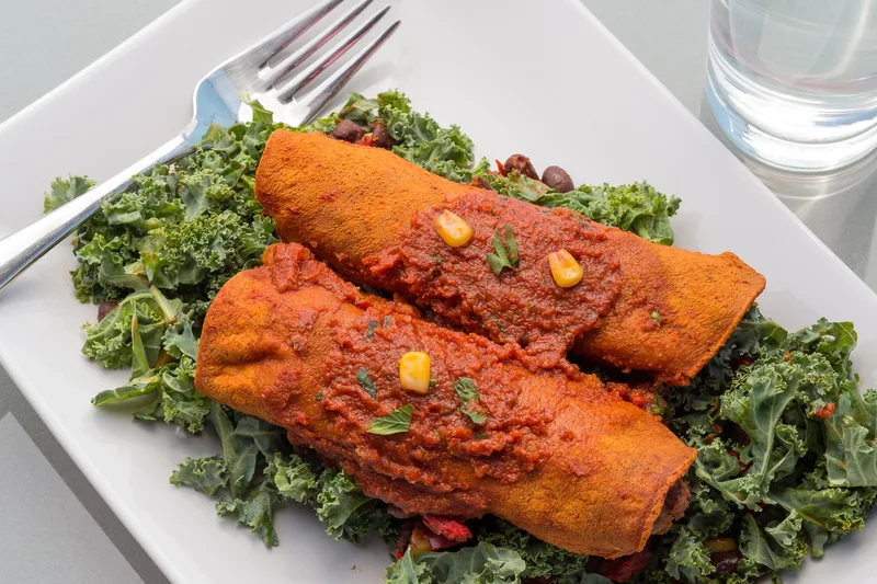 Two enchiladas covered in red chile sauce on a bed of kale