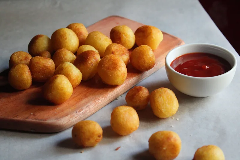 Fried potato balls on a board with a bowl of ketchup