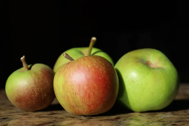 Green Granny Smith and red apples side by side on a wooden table