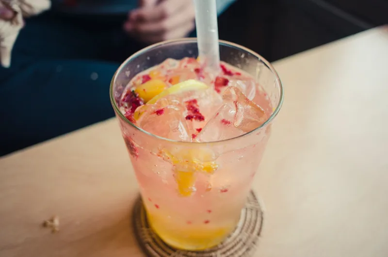 A glass of peach-coloured lemonade with fruit and ice