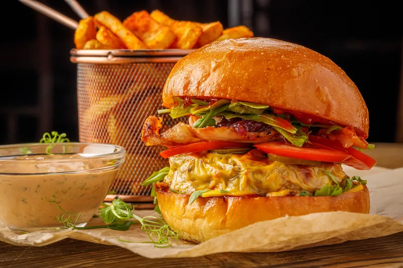 A burger served beside a bowl of creamy sauce